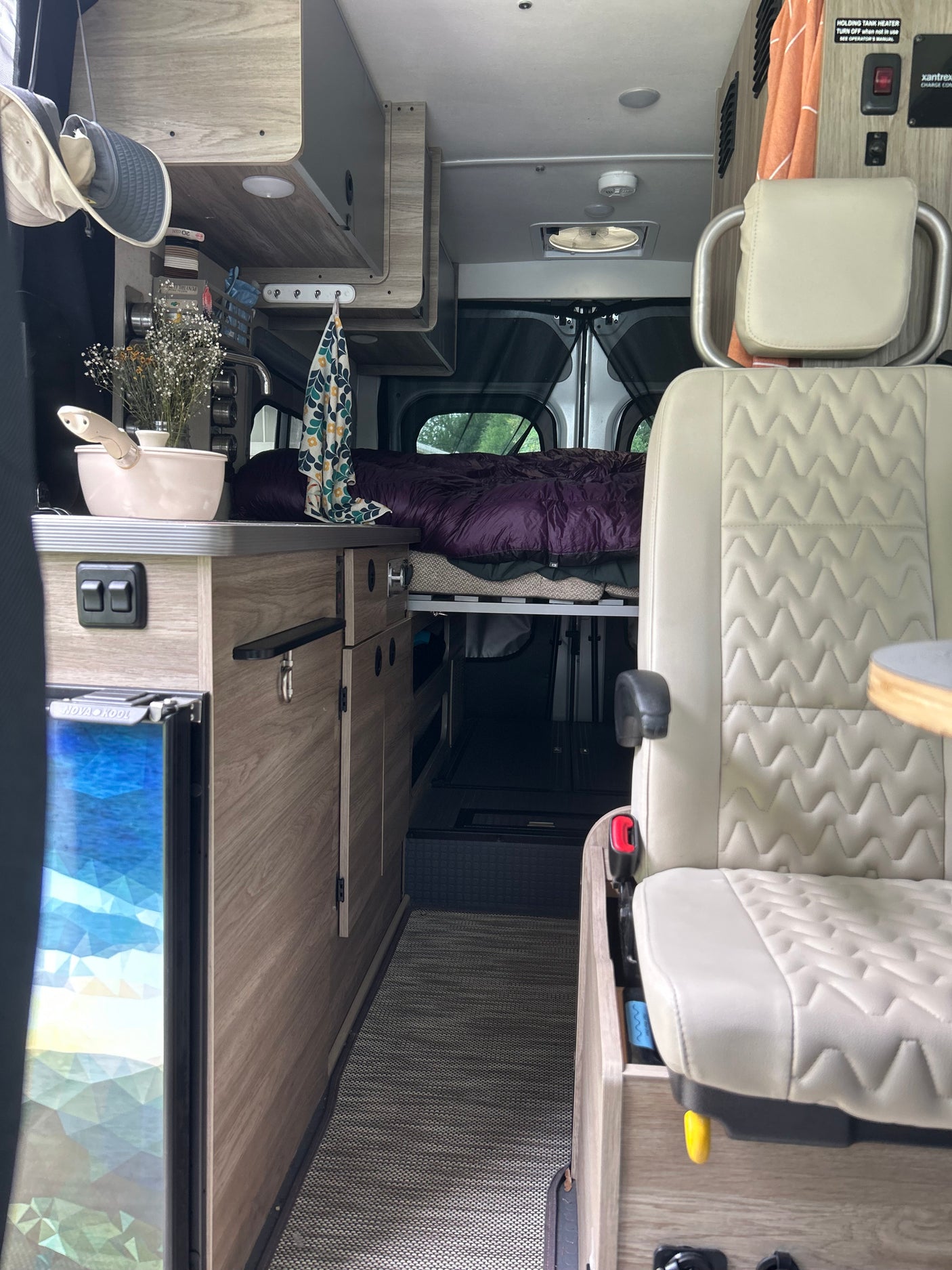 Step inside this cozy RV rental's interior, featuring a compact kitchen, comfortable bed, and front passenger seat.