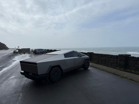 Sleek Tesla Cybertruck on a wet coastal road overlooking a stormy ocean. Forget an RV rental, this is modern exploration.