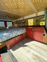 This RV rental's interior features a patterned bed, red storage cabinets, a small sink, and a unique woven ceiling.
