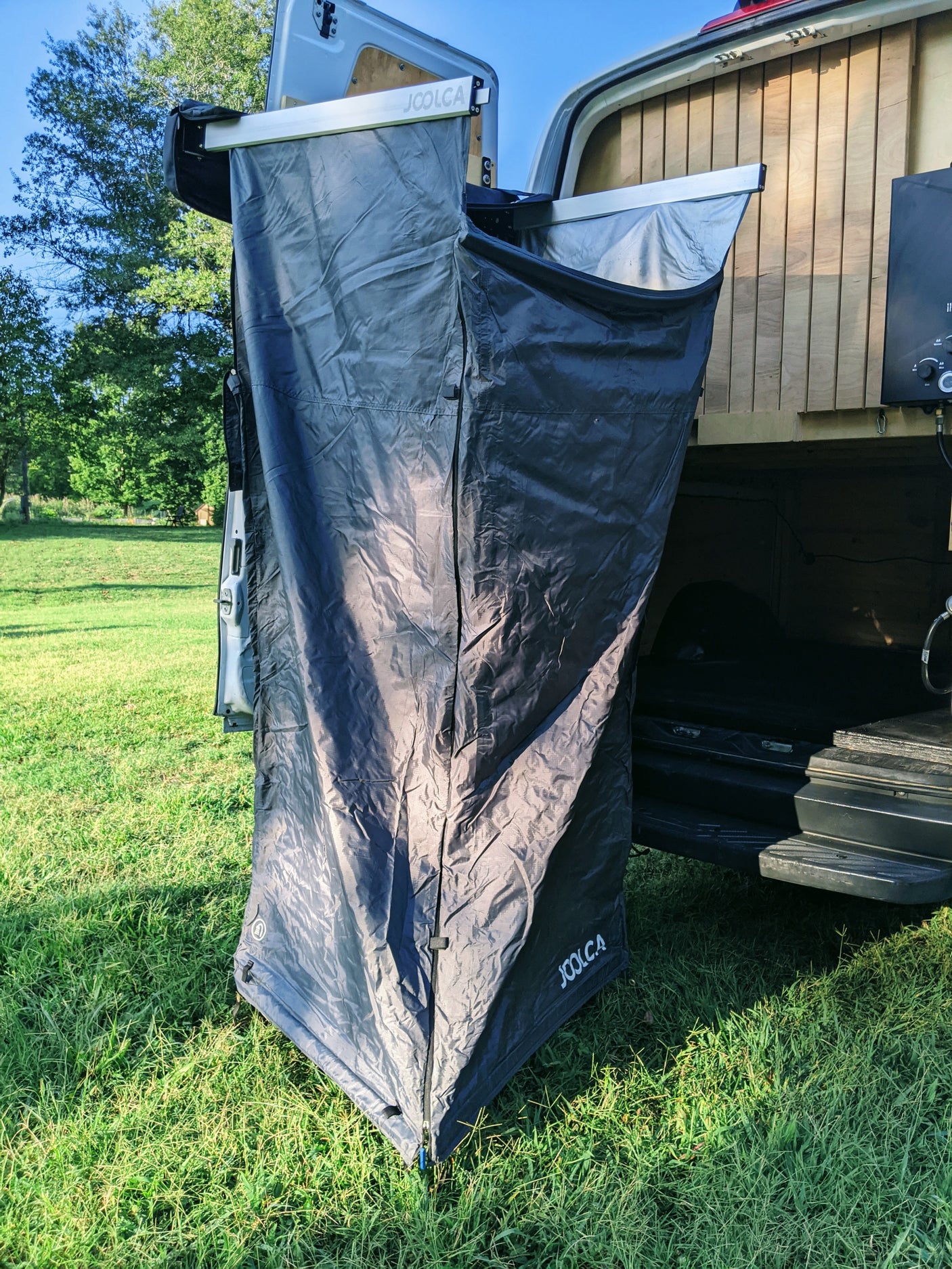 RV rental's Joolca outdoor shower privacy tent extended from the van's rear, ready in a grassy field.