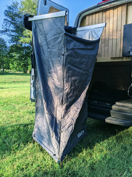 RV rental's Joolca outdoor shower privacy tent extended from the van's rear, ready in a grassy field.