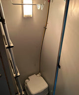 This RV rental features a small bathroom with a portable toilet and a bunk bed ladder.