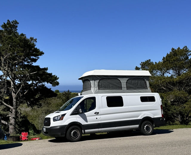 parked at a sunny campground against stunning red rock mountains.|White pop-top campervan