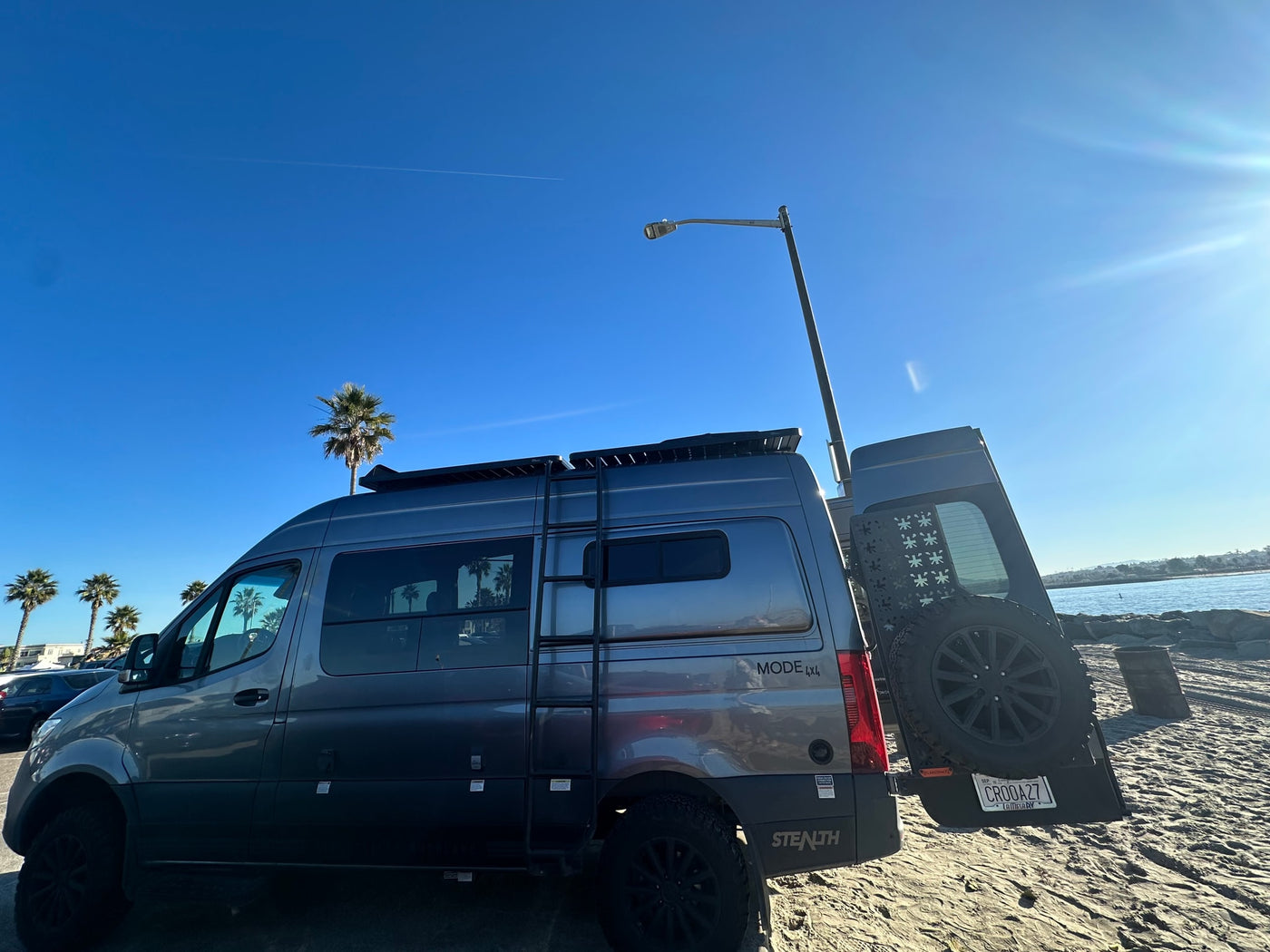 Gray custom camper van, a perfect RV rental for beach adventures, parked on sand by the water. — photo 12