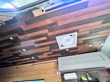 See a cozy RV rental interior: alternating wood ceiling planks, bright lights, central fan, and wall-mounted storage.