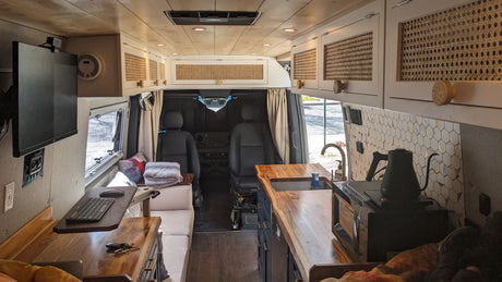 RV rental van interior with a bright, custom-built design. Features a wood-paneled ceiling, modern kitchen, and cozy living area.