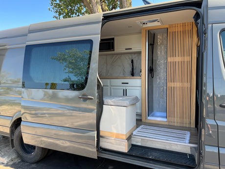 View inside a grey camper van, an ideal RV rental. It features a modern kitchen, shower, and slatted wood accents.