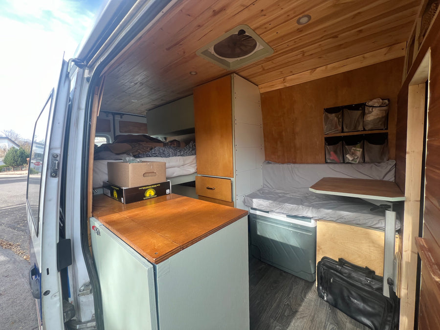 Inside a custom RV rental: A well-designed camper van interior with a bed, wood accents, and seating for adventures.
