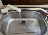 An RV rental kitchen features a stainless steel sink with running water from a white faucet, ready for use on your trip.
