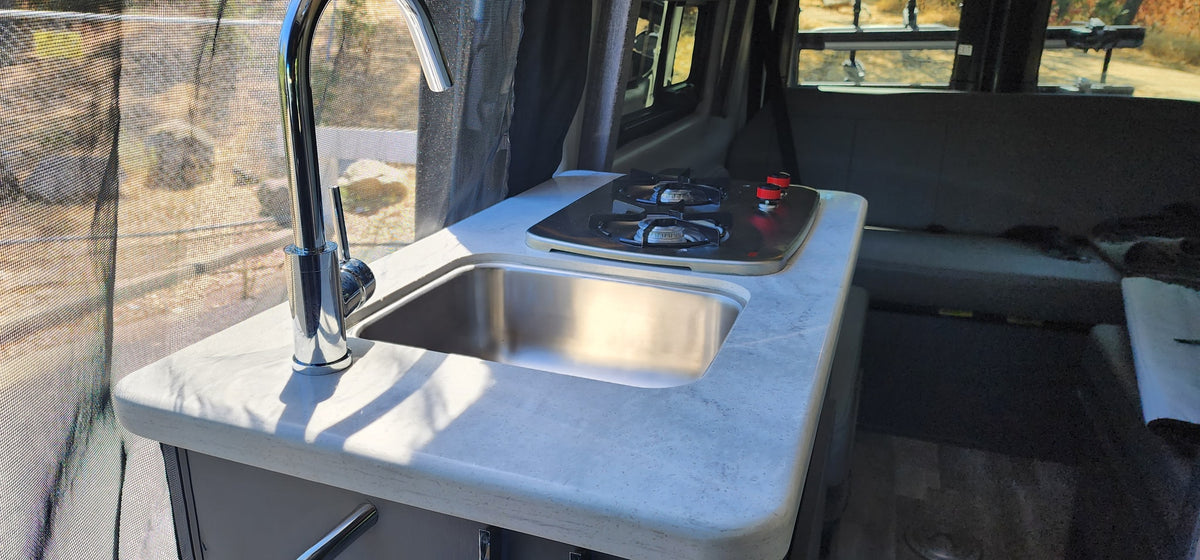 Compact kitchen in an RV rental, featuring a chrome faucet, stainless steel sink, and two-burner stove by a screened window. — photo 4