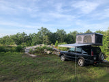 Black SUV with a rooftop tent and awning, ready for an overlanding adventure. A unique RV rental experience in nature.