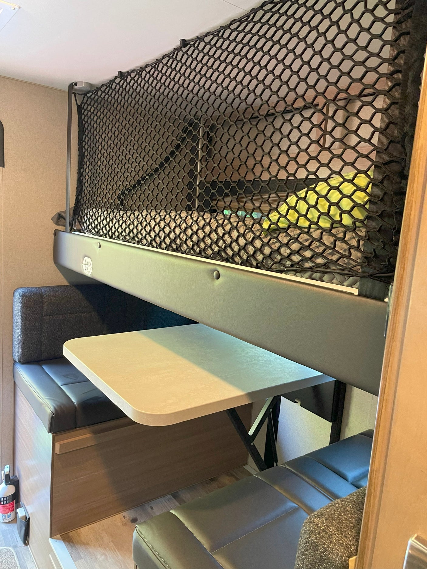 This RV rental interior features a cozy bunk bed with a safety net and a dinette area with bench seating and a table.