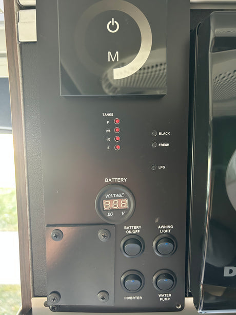 RV control panel in an RV rental, displaying tank levels (fresh, black, LPG), battery voltage, & switches for awning, inverter, water pump.