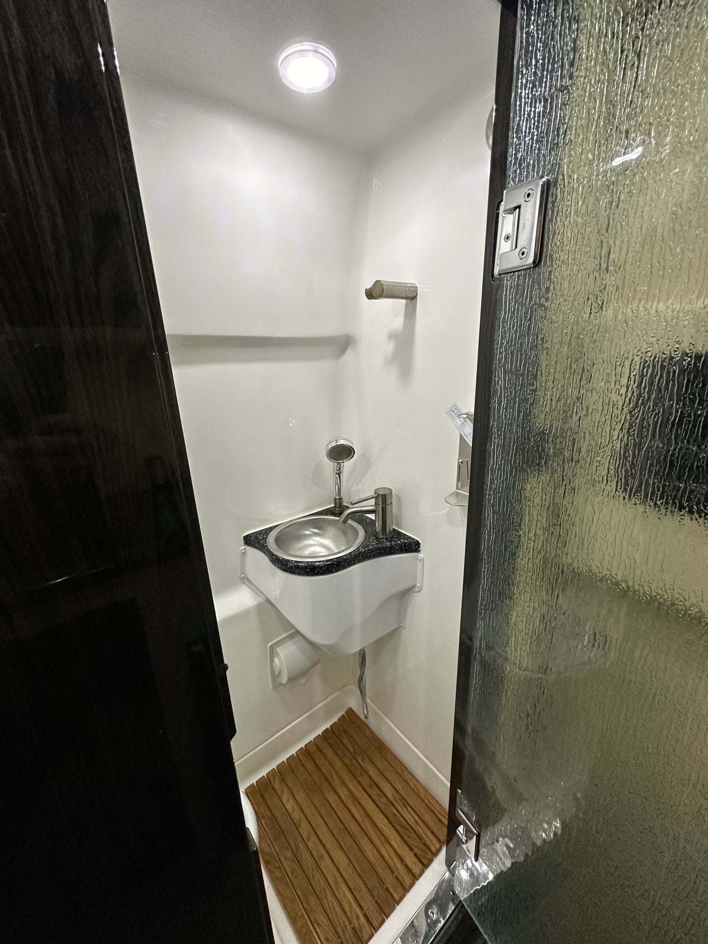 Step inside this modern RV rental's compact wet bath, featuring a corner sink, shower, and wooden floor mat for convenient travel.