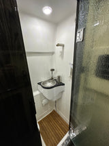 Step inside this modern RV rental's compact wet bath, featuring a corner sink, shower, and wooden floor mat for convenient travel.