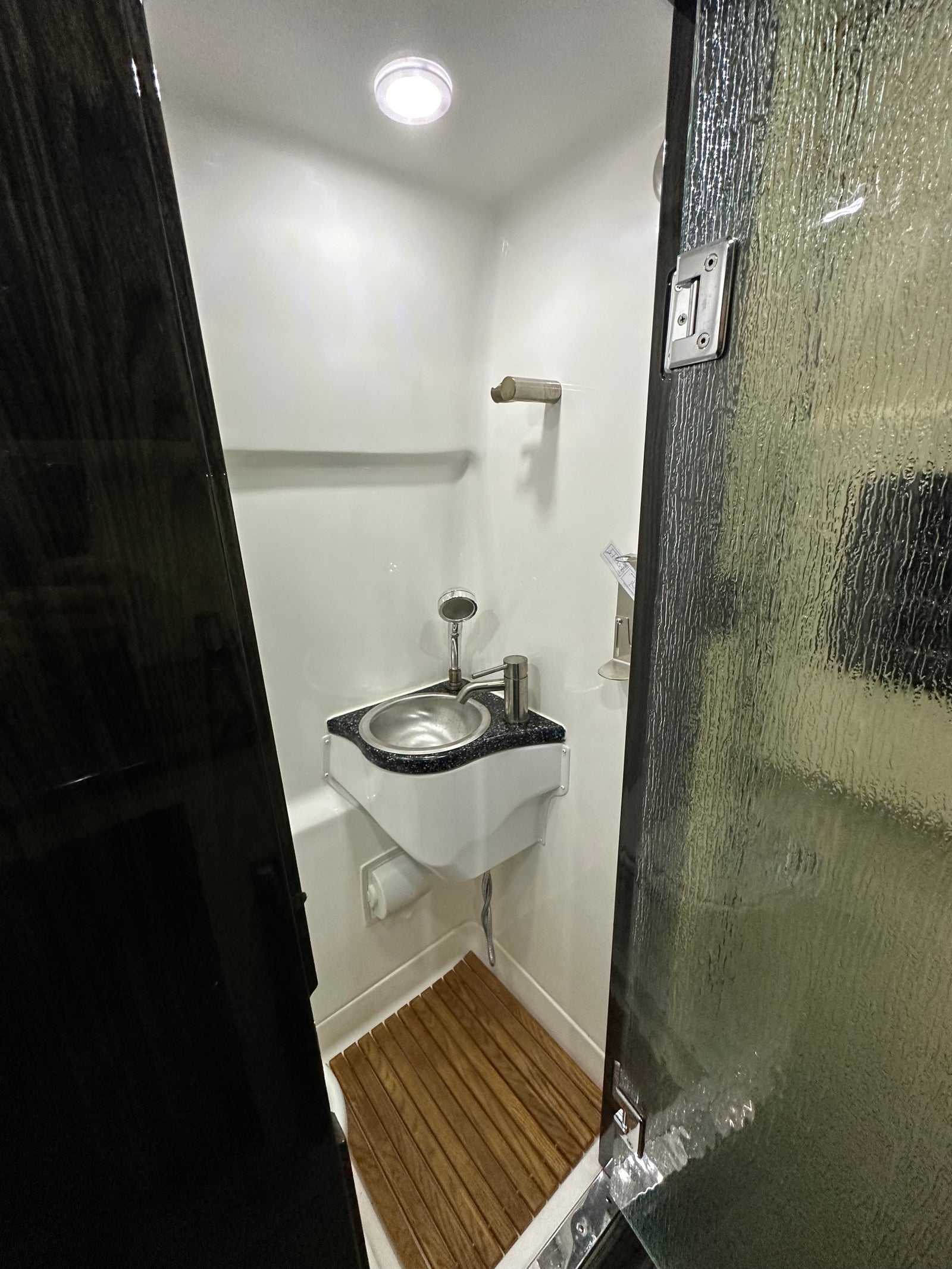 Step inside this modern RV rental's compact wet bath, featuring a corner sink, shower, and wooden floor mat for convenient travel.