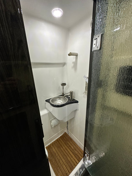 Step inside this modern RV rental's compact wet bath, featuring a corner sink, shower, and wooden floor mat for convenient travel.