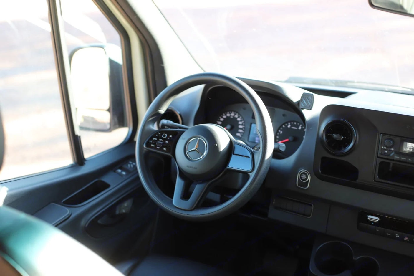 RV rental interior: Mercedes-Benz steering wheel, dashboard, and door panel with controls from the driver's perspective.