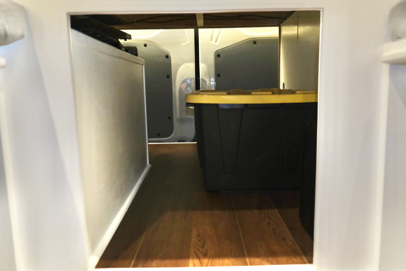 RV rental storage: A black bin with a yellow lid and a silver appliance inside a compact storage bay.