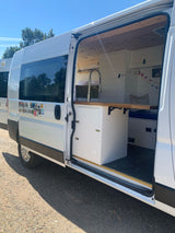 White RV rental conversion van with open side door revealing a custom interior, including a kitchen and bed area, for van life.