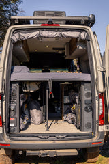 This rv rental camper van's open rear reveals a raised bed, ample gear storage, and water/power control panels.