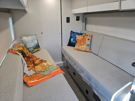 Cozy RV rental interior with stylish bench seating, Van Gogh art pillows, and a vibrant throw blanket for a comfortable stay.
