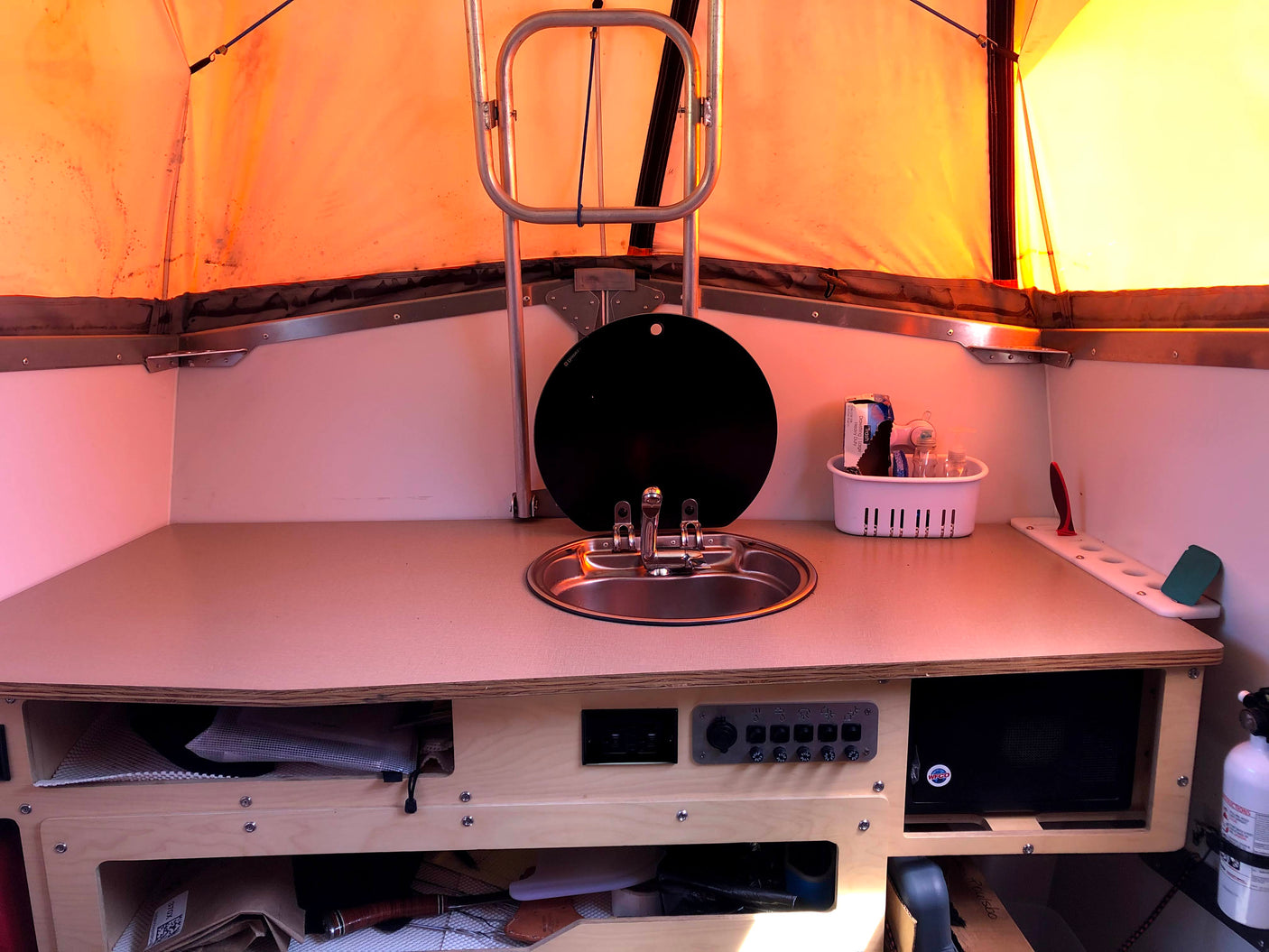 RV rental interior shows a compact pop-up camper kitchen with a sink, counter space, and utility controls for convenience.