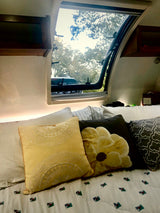 Cozy RV rental interior featuring a bed with decorative pillows and an open window revealing lush trees. #rvrental #camping #travel