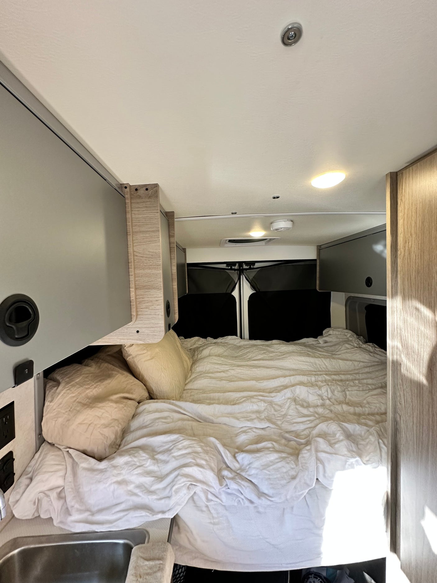 Comfortable RV rental interior with a large bed, overhead storage, and a sink, perfect for a road trip.