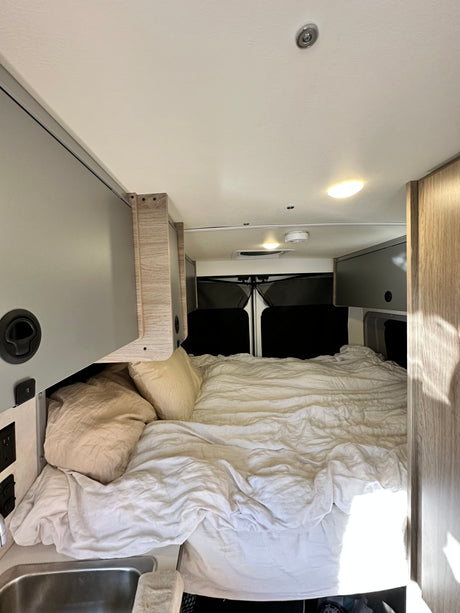 Comfortable RV rental interior with a large bed, overhead storage, and a sink, perfect for a road trip.