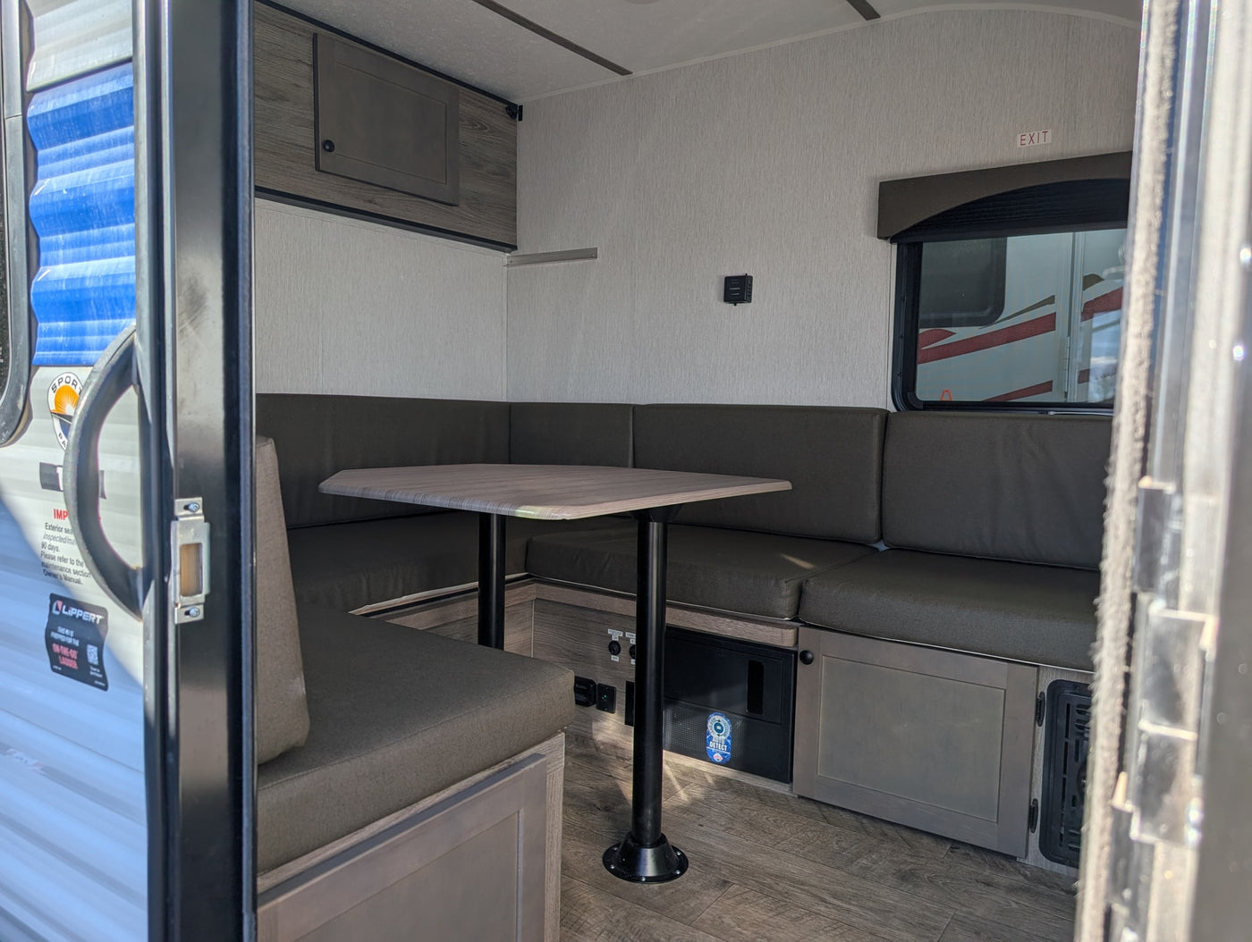 This RV rental interior features a functional dinette with U-shaped seating, a central table, and a window with an exit sign. — photo 19