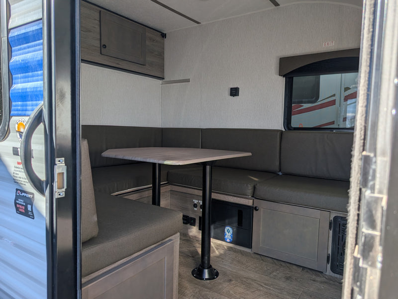 This RV rental interior features a functional dinette with U-shaped seating, a central table, and a window with an exit sign. — photo 19