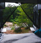 View from an **RV rental** bed looking out at a scenic river, green trees, and a large rock by the water.