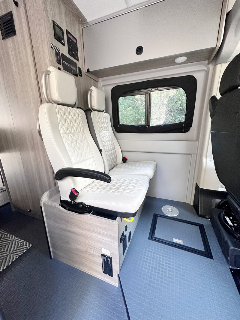  showing a glimpse of its cozy interior amidst trees.|Inside a modern RV rental: white quilted seating — photo 6
