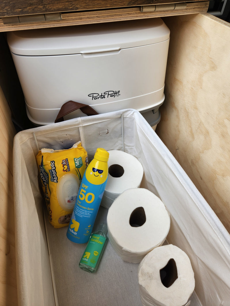RV rental essentials: Porta Potti, toilet paper, wipes, sunscreen, and hand sanitizer stored in a wooden compartment. — photo 14