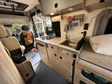 Inside an RV rental: a well-equipped camper van kitchen (sink, stove, storage), comfy bed, and organized driver's area for adventures.