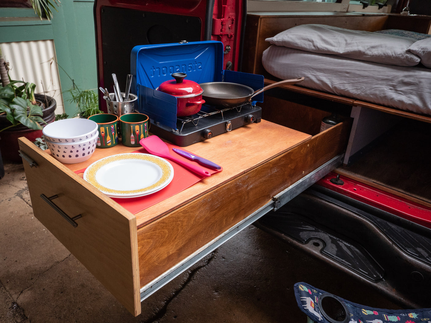 Compact RV rental kitchen setup: a pull-out drawer with stove, cookware, and dishes, ready for adventure.