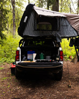 An RV rental setup: truck with rooftop tent and tailgate kitchen, ready for serene forest camping.