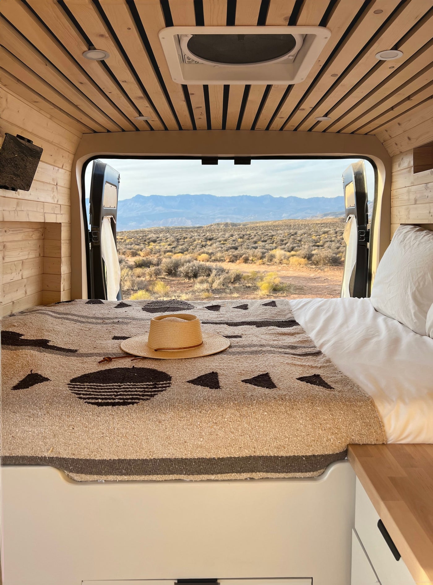 Cozy RV rental interior with a bed and hat, offering stunning desert mountain views from the back of the van. Perfect for travel. — photo 7