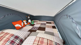 A cozy pop-top bed in an RV rental, with a patchwork quilt, plaid pillows, and cute stuffed animals.