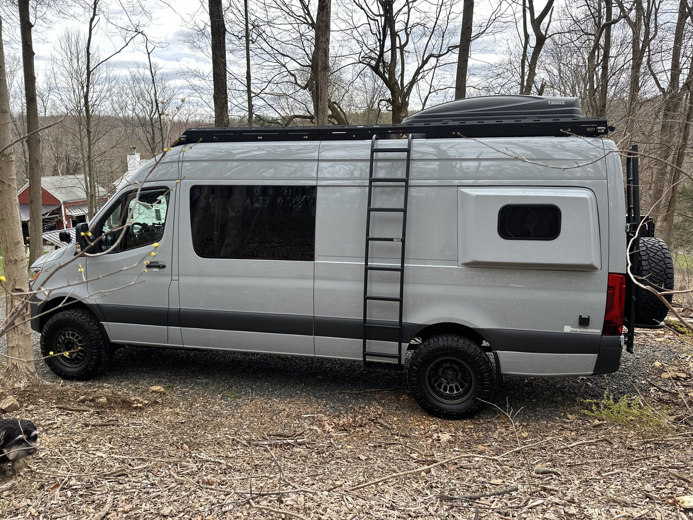 Gray Sprinter camper van, ideal for rv rental adventures, featuring a roof rack, ladder, and off-road tires, parked outdoors.