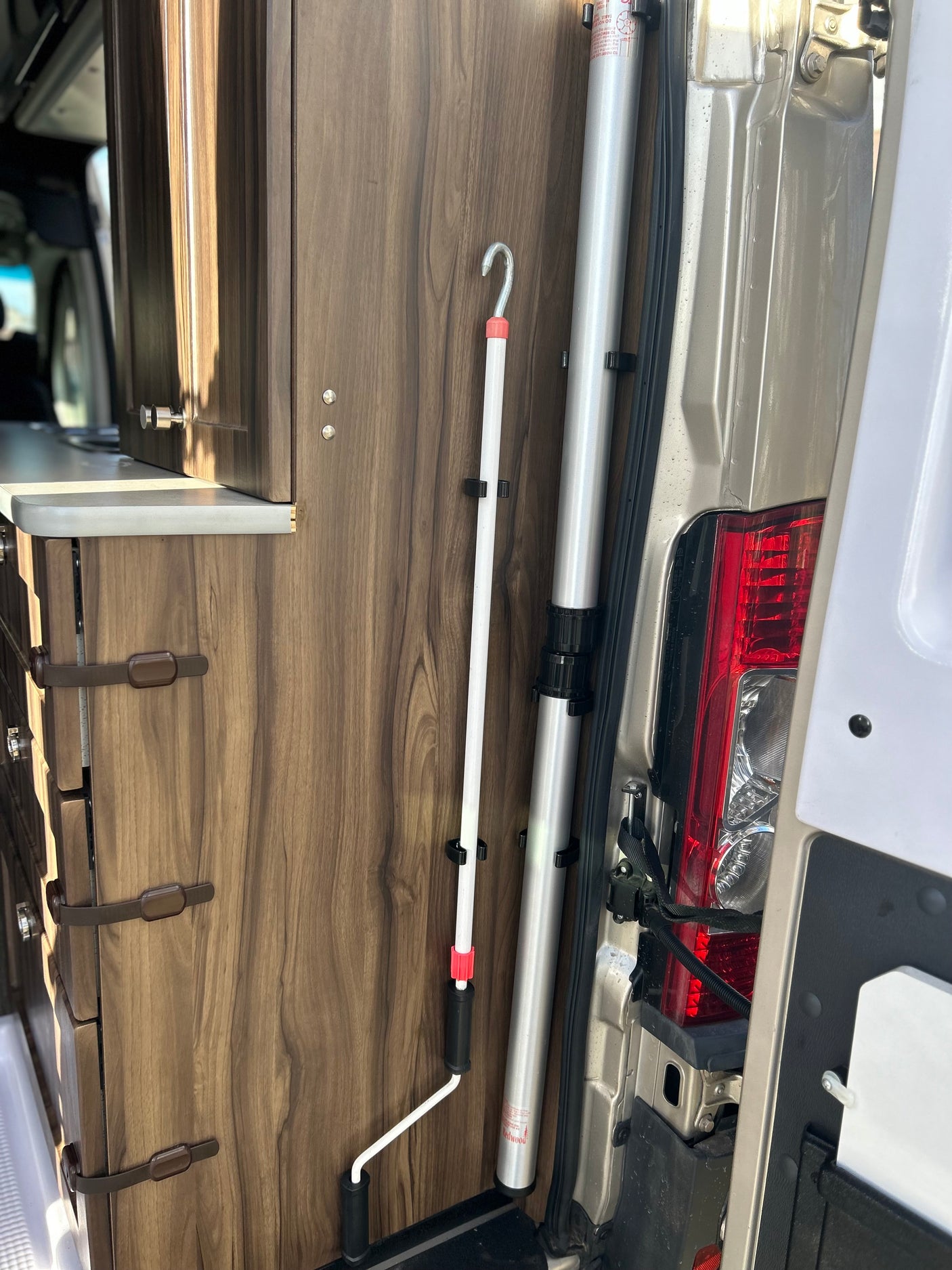 RV rental interior: wood cabinets, countertop, and neatly stored vertical poles (white awning crank pole, silver support pole).