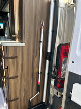 RV rental interior: wood cabinets, countertop, and neatly stored vertical poles (white awning crank pole, silver support pole).