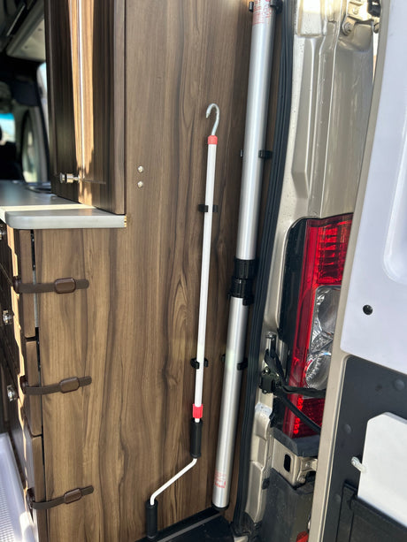 RV rental interior: wood cabinets, countertop, and neatly stored vertical poles (white awning crank pole, silver support pole).