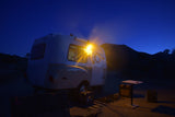 This cozy RV rental brightens a desert night campsite. A small camper and gear are illuminated under a dark blue sky.