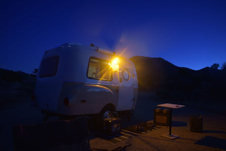 This cozy RV rental brightens a desert night campsite. A small camper and gear are illuminated under a dark blue sky.