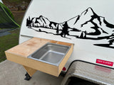 RV rental showing an attached wooden outdoor kitchen with a stainless steel sink and counter, beside a mountain decal.