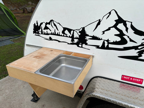 RV rental showing an attached wooden outdoor kitchen with a stainless steel sink and counter, beside a mountain decal.