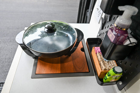 RV rental's compact kitchen featuring an electric skillet, wooden base, and wall-mounted organizer with soap, sugar packets.