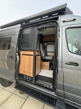 Grey RV rental's open side door reveals a modern camper van interior with wooden cabinetry and seating.